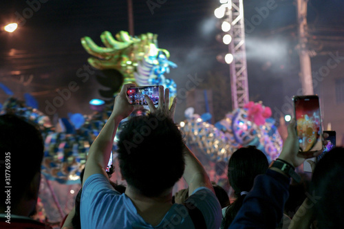 Selective focus on hands hold the mobile phone and record the clip of show with motion blurred dancing dragon performance in background