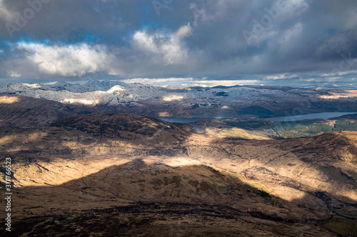 Dramatic winter view from Ben Lomond towards Loch Lomond and the peaks of Arrochar Alps in Scottish Highlands.