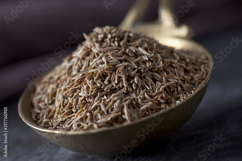 Brass spoon with cumin seeds on textile, close up photo