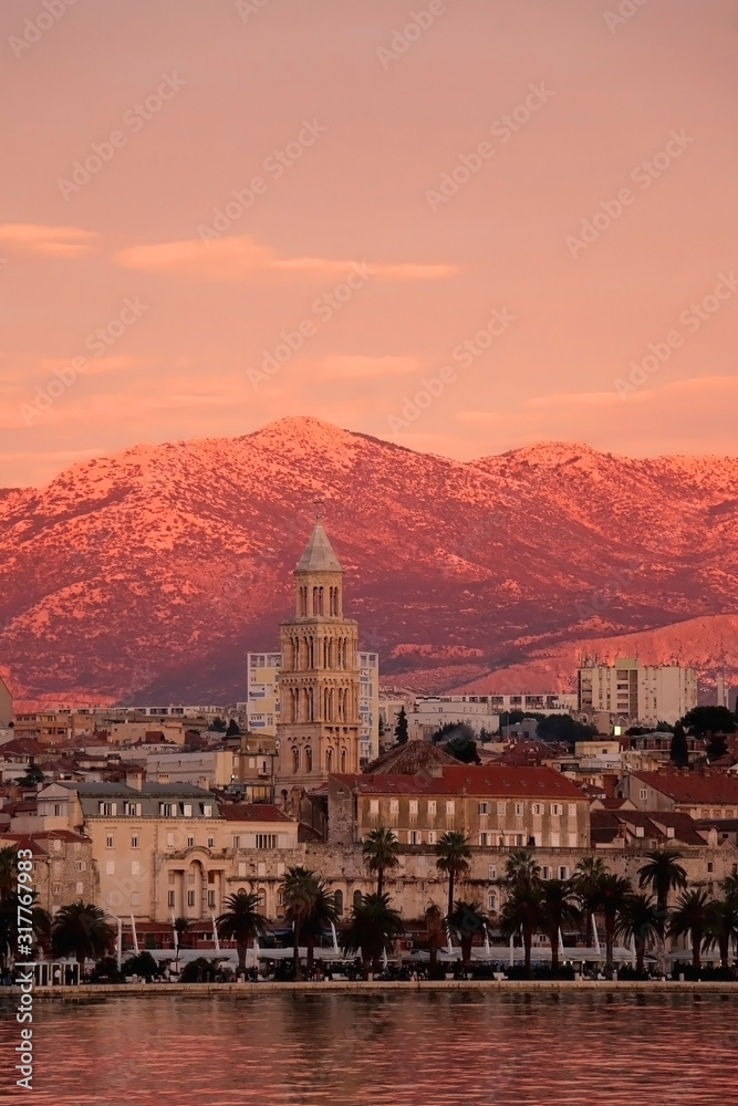 Historic architecture on Riva promenade in Split, Croatia with landmark Saint Domnius bell tower, illuminated by beautiful pink sunset light.