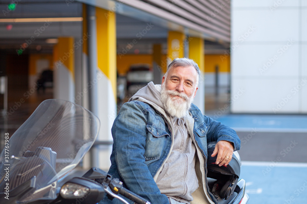 Elderly man with white beard resting sitting on his scooter motorcycle smiling