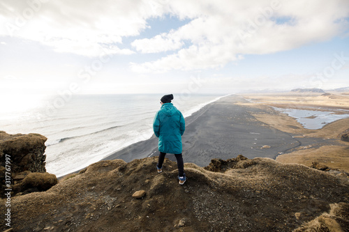 male traveler in green clothes and sitting near a cliff view of a black beach and the Atlantic Ocean in Iceland