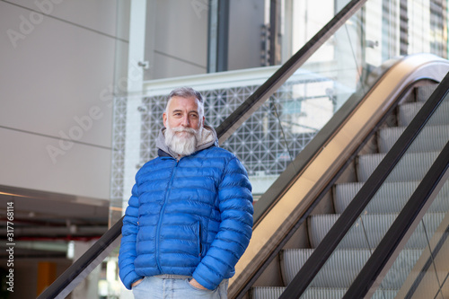 Man with white beard going down the escalator with his hands in his pockets