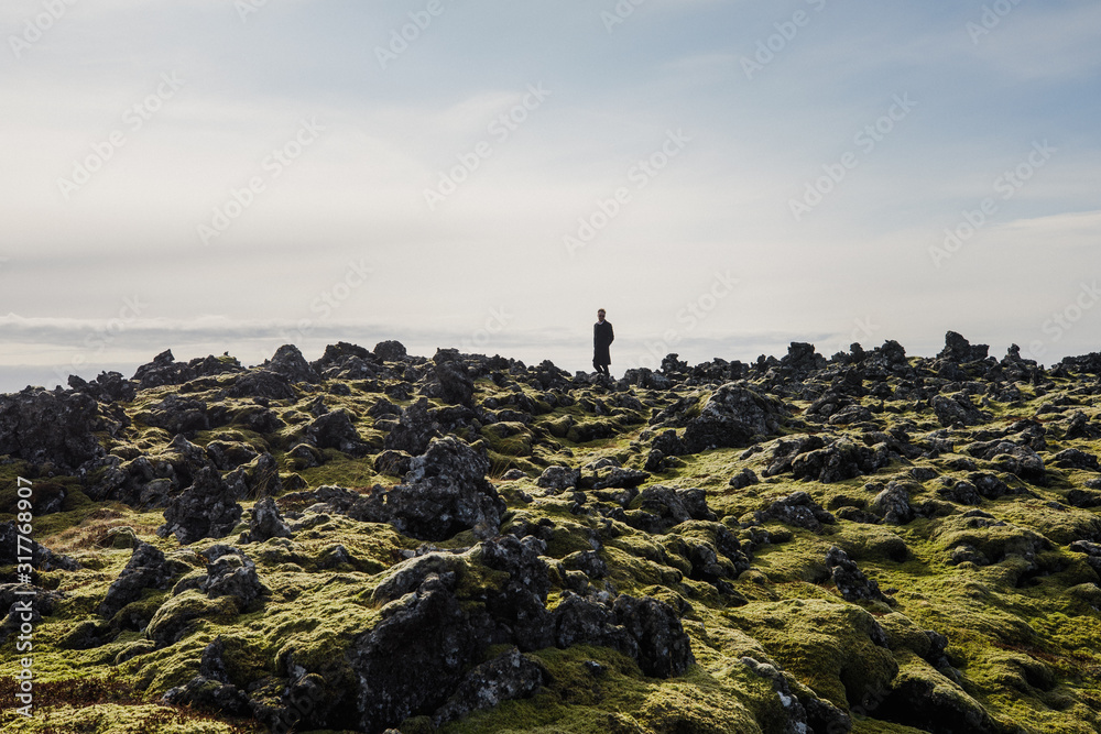 young man in black clothes stand on lava rock