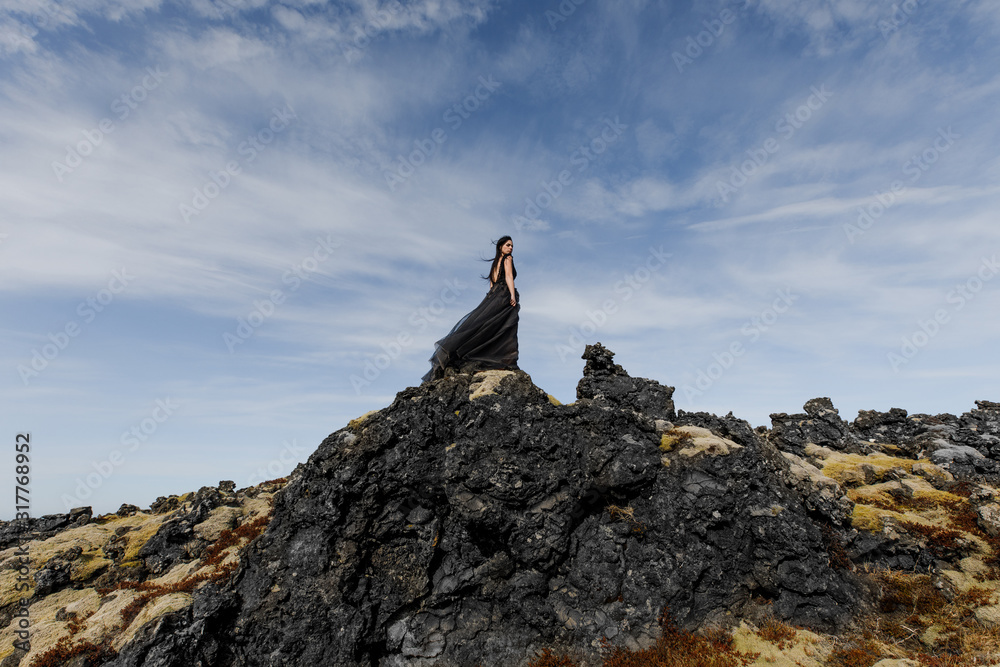 young wedding bride in black clothes stand on lava rock