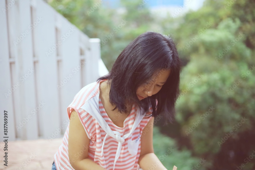 Young asian woman in casual clothes standing alone and looking down on the balcony against burred green natural background Young asian woman in casual clothes standing alone and looking down on the balcony against burred green natural background