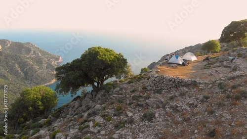 Sporty people sitting near their tents and observing the breathtaking sunset illuminating the picturesque mountain landscape