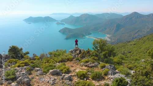 Aerial shot flying over man standing on the edge of a cliff in the summer. Drone shot
