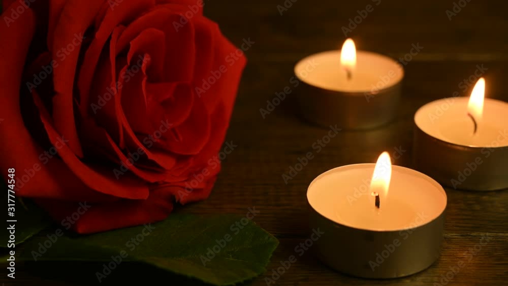 a red rose lies on a table and three candles are burning a red rose lies on a table and three candles are burning