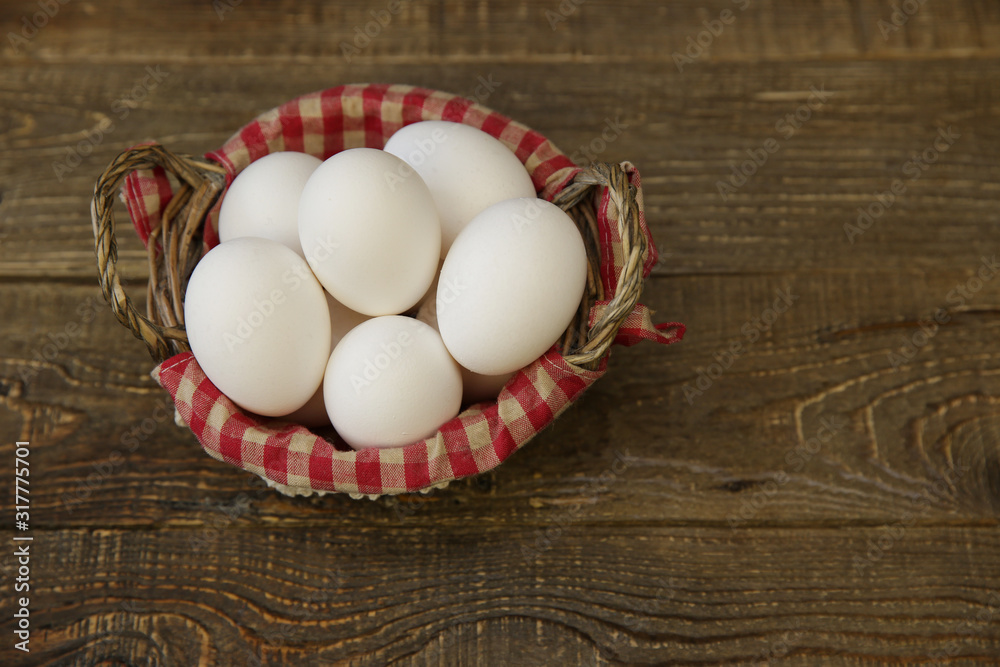 Close-up organic white eggs in a basket with a decorated checkered napkin on a wooden rustic background. Farm products. Easter holiday.