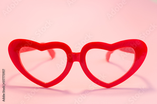 Red glasses in the shape of hearts on a pink background.