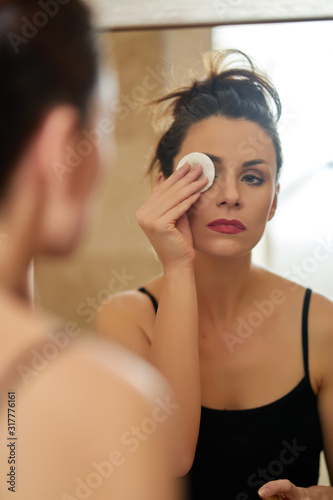 Beautiful woman washes away makeup in front of mirror