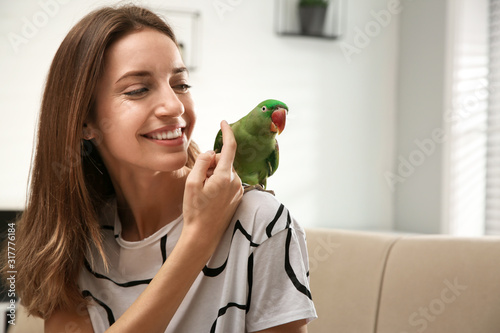Fotografie, Obraz Young woman with cute Alexandrine parakeet indoors