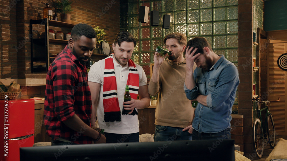 Obraz premium Four friends watching american football game, showing frustration. Group of young friends watching a football match, cheering and drinking beer, disappointed after they lost the match. Negative