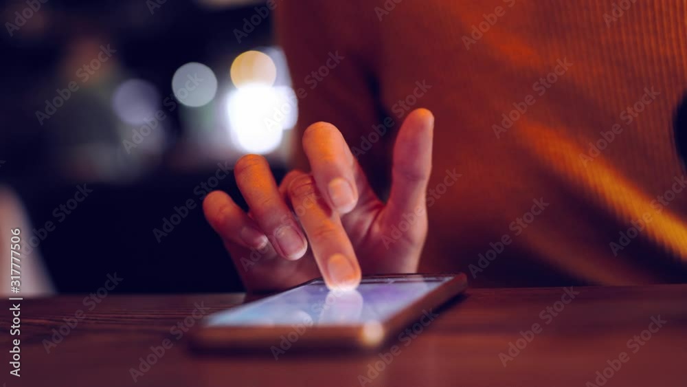 Phone - closeup female hand scrolling using app on smart phone in caffee. Closeup of hand using smartphone indoorsdoors. Mobile cell phone close up.