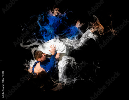 The two judokas fighters fighting men on smoke background