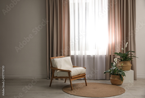 Comfortable armchair near window with elegant curtains in room