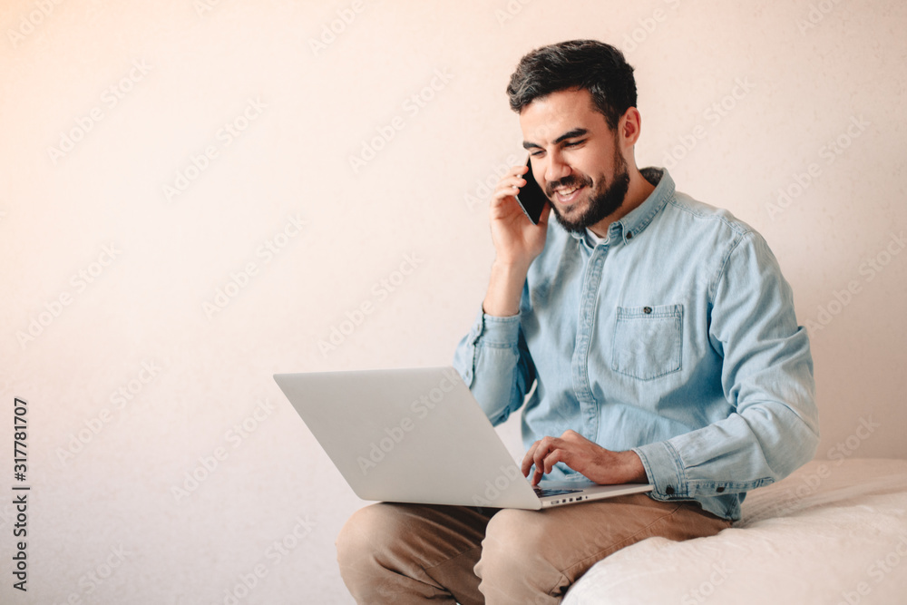 Happy man talking on smart phone while using laptop computer at home Happy man talking on smart phone while using laptop computer at home