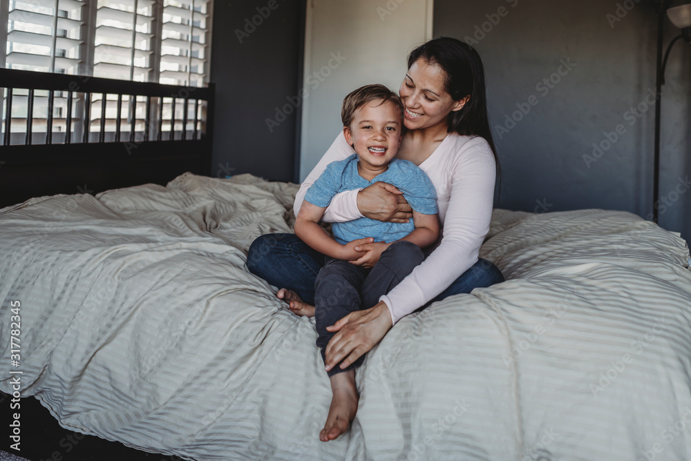 Smiling mom holding happy 5 yr old son on comforter near window Smiling mom holding happy 5 yr old son on comforter near window