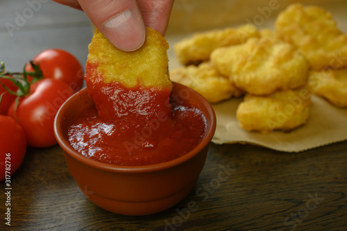 hand takes nuggets and dips it in tomato sauce photo