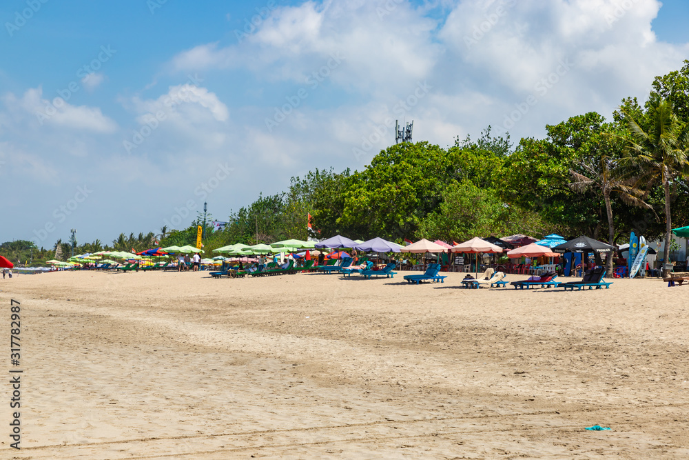 KUTA, BALI / INDONESIA - NOVEMBER 8, 2019: Kuta beach in Bali. Wide sandy beach with many sunbeds and umbrellas. Best place for surfing.