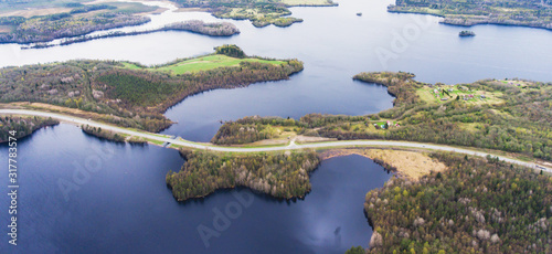 Beautiful view from a road going through the beautiful lake and forest, surrounded with water on both sides, shot above from drone, aerial vibrant picture