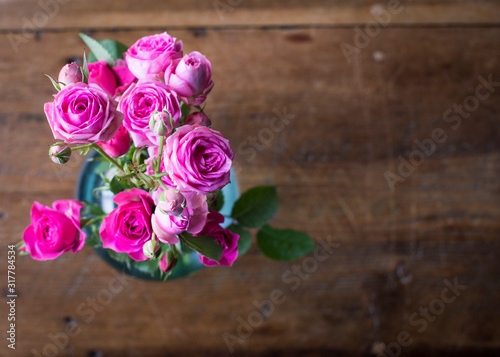 Hot pink miniature roses in a blue glass vase on dark vintage table.