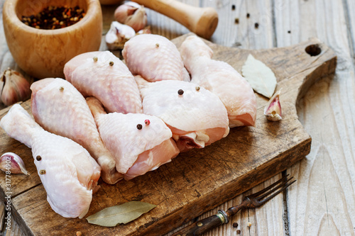 raw chicken legs on a wooden board on a table with seasonings for cooking