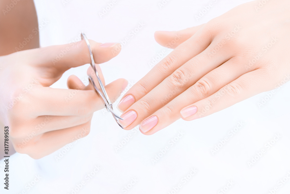 Closeup of female hands are holding scissors. Young woman is cutting her nails, making herself hygienic manicure. Tool for giving nail plate certain shape and length. Personal hygiene and care concept Closeup of female hands are holding scissors. Young woman is cutting her nails, making herself hygienic manicure. Tool for giving nail plate certain shape and length. Personal hygiene and care concept