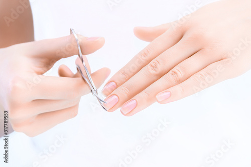 Closeup of female hands are holding scissors. Young woman is cutting her nails  making herself hygienic manicure. Tool for giving nail plate certain shape and length. Personal hygiene and care concept
