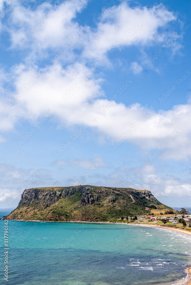 Stanley, Tasmania, Australia - December 15, 2009: Portrait of The Nut volcanic plug under blue cloudscape.  Blue ocean in front and some white houses of town.