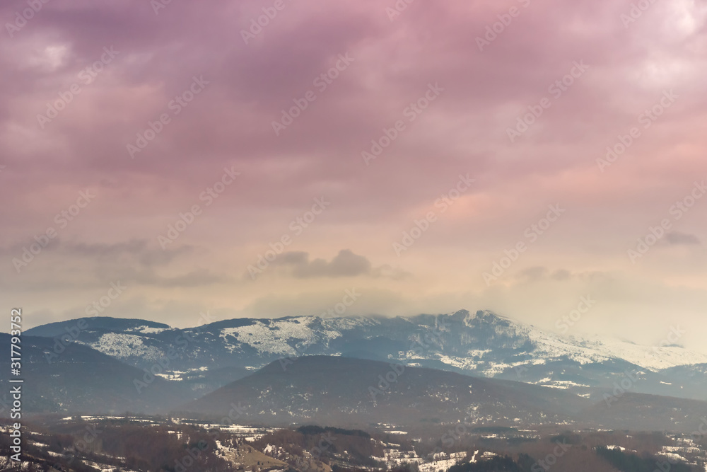 Distant mountain covered in snow and fog and beautiful, purple and golden sunset sky