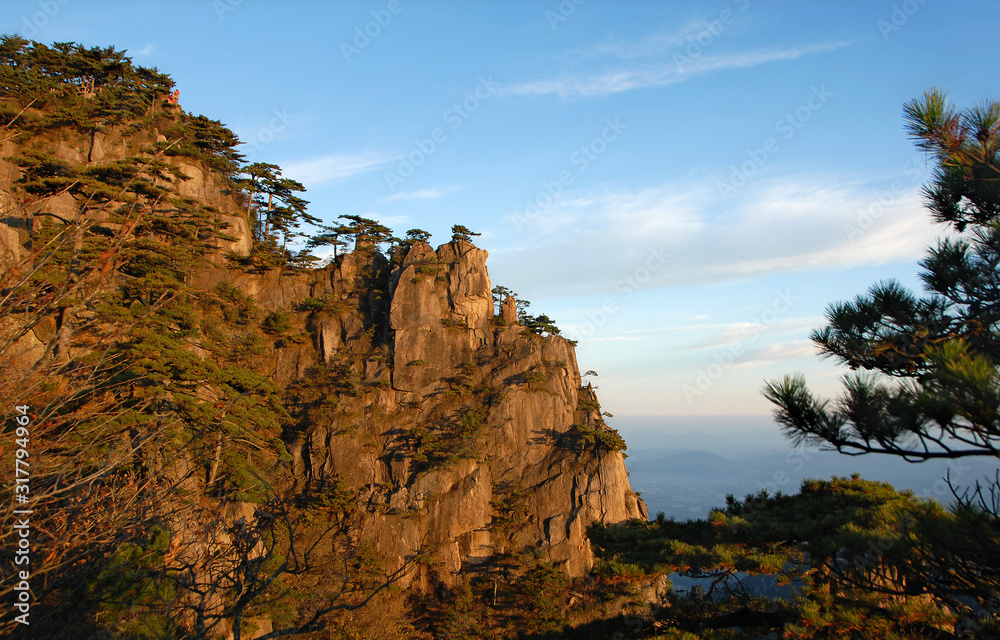 Huangshan Mountain in Anhui Province, China. View at sunrise near Stone Monkey Watching the Sea viewpoint with rocky cliffs and pine trees. Scenic view of peaks and trees on Huangshan Mountain, China.