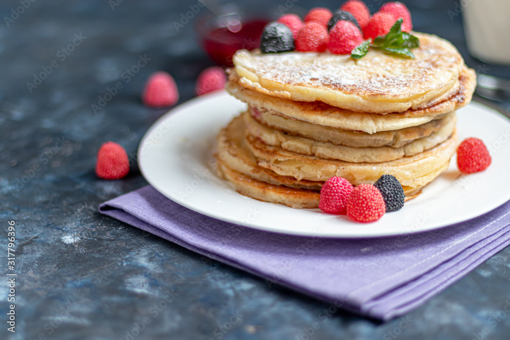 A stack of delicious pancakes with raspberries, blackberries and blueberries. On a dark stone background. Sprinkled with icing sugar and decorated A stack of delicious pancakes with raspberries, blackberries and blueberries. On a dark stone background. Sprinkled with icing sugar and decorated