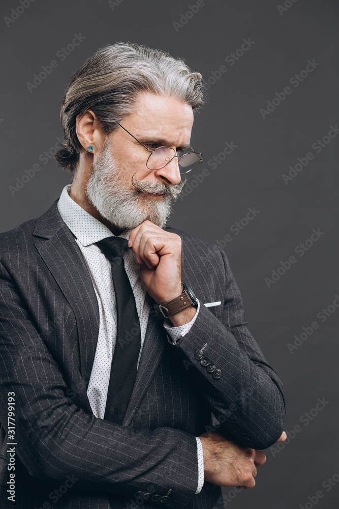 Business and fashionable mature bearded man in a gray suit holding beard and thinking Business and fashionable mature bearded man in a gray suit holding beard and thinking