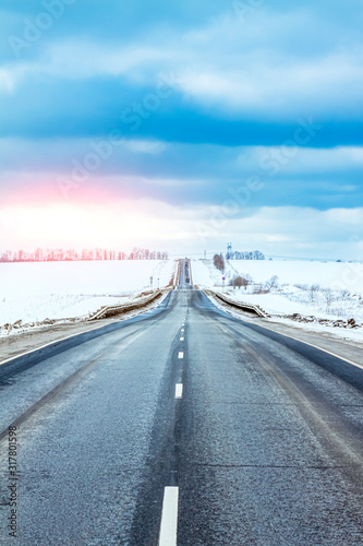 Winter road going over the horizon. Blue clouds above the road.