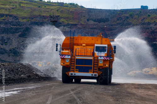 Heavy truck pours the road with water in the iron ore quarry. Dust removal, protection of the environment. Irrigation of the road from dust. The World’s Largest Sprinkler Truck