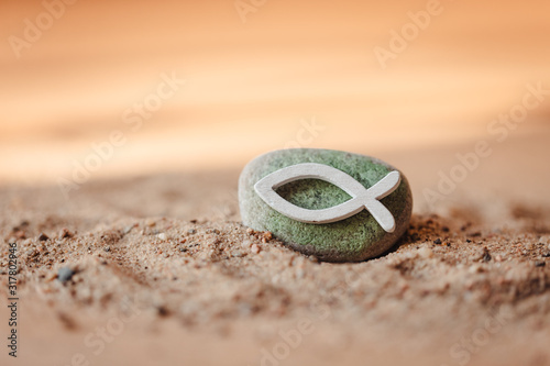 Kommunion, Konfirmation, Firmung, Taufe - weißer Fisch aus Holz auf grün bemalten Stein im Sand photo