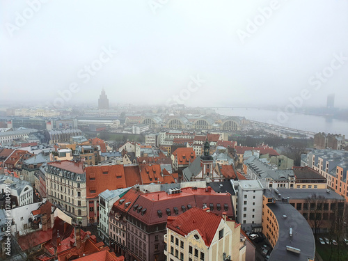 Riga city in winter autumn. Latvia capital. Old Riga with fog. Aerial photo. Top view of the city from Peter church. Many red roofs, sheds for airship, sightseengs, place of interests, tourists..
