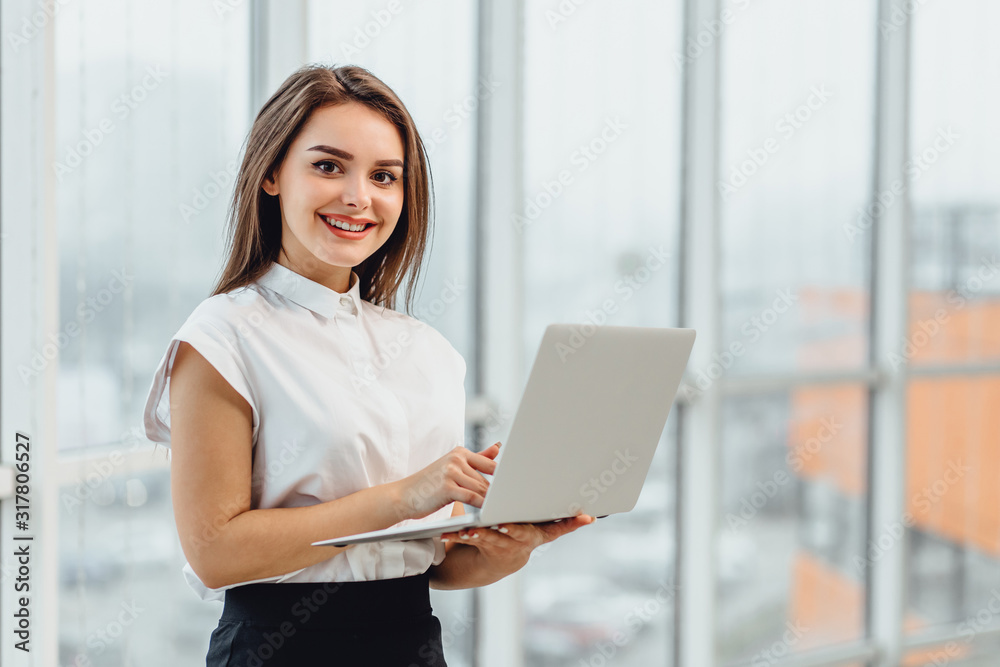 Joyful business woman standin in office, holding laptop. Joyful business woman standin in office, holding laptop.