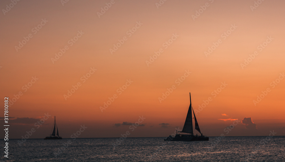 Enjoying the sunset while sailboats pass by the sunset horizon.