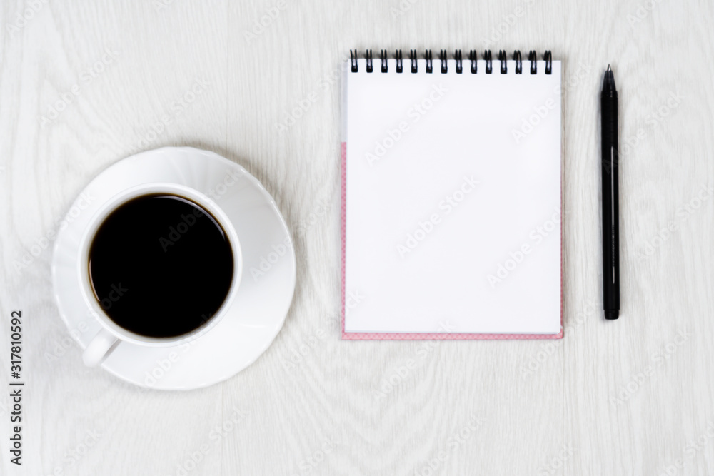 White cup with coffee on a white table with a notebook and pen White cup with coffee on a white table with a notebook and pen