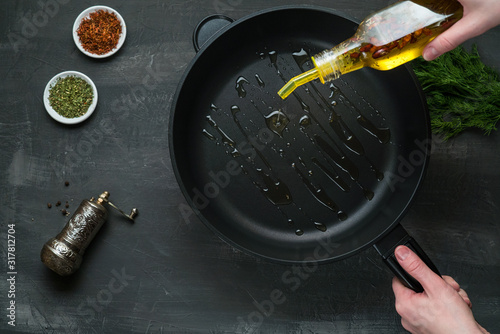 Man pouring cooking oil on the frying pan - Top View on a dark background