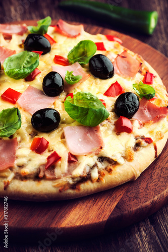 Pizza with ham, black olives, red pepper and fresh basil.