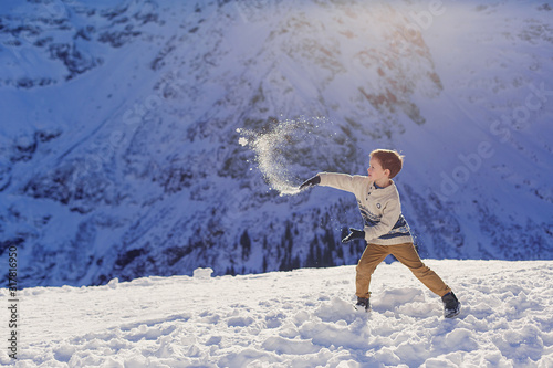 Child boy 5 years in a winter sweater plays snowballs in the mountains. Snow peaks on background. Beautiful landscape of the Alps. Ski resort. Children's game fun vacation holidays leisure. Childhood