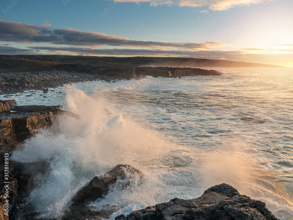 Powerful wave crashes at stones creating splash of water, West coast of Ireland, Sunset time, Atlantic ocean.