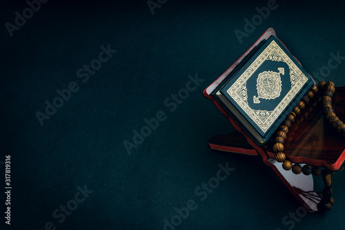 Holy Al Quran with written arabic calligraphy meaning of Al Quran and tasbih or rosary beads on black background. Selective focus and crop fragment photo