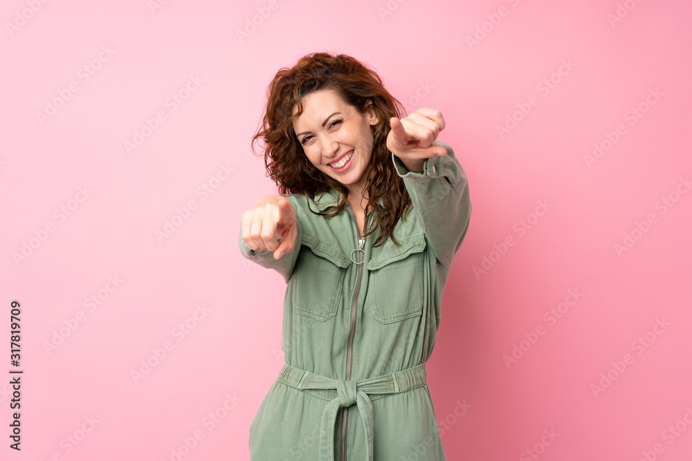 Young pretty woman over isolated pink background points finger at you while smiling Young pretty woman over isolated pink background points finger at you while smiling
