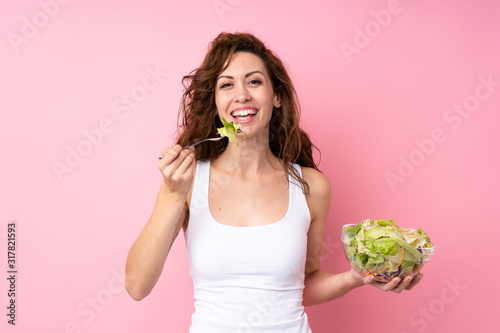 Young woman with curly hair holding a salad over isolated pink background