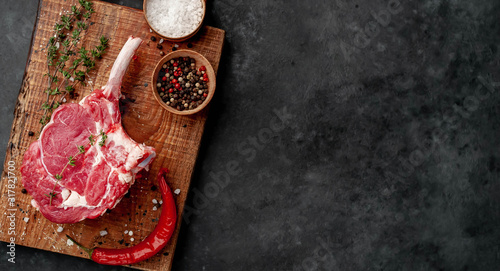 raw beef steak, beef tomahawk with spices, thyme on a stone background. with copy space for your text